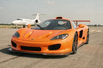 McLaren F1 en orange papaye garé sur un tarmac d'aéroport privé, vue grand angle au niveau du sol mettant en valeur la carrosserie en fibre de carbone